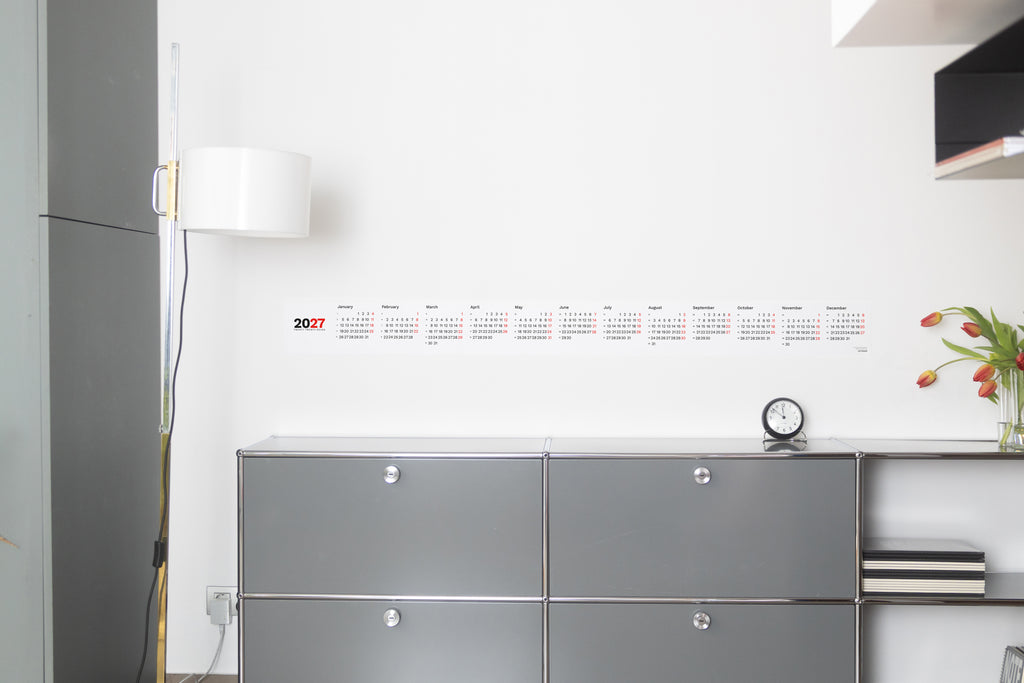 2027 Horizontal Calendar by Octàgon Design. The calendar placed on top of a piece of USM furniture and besides the Arne Jacobsen clock and Mila lamp