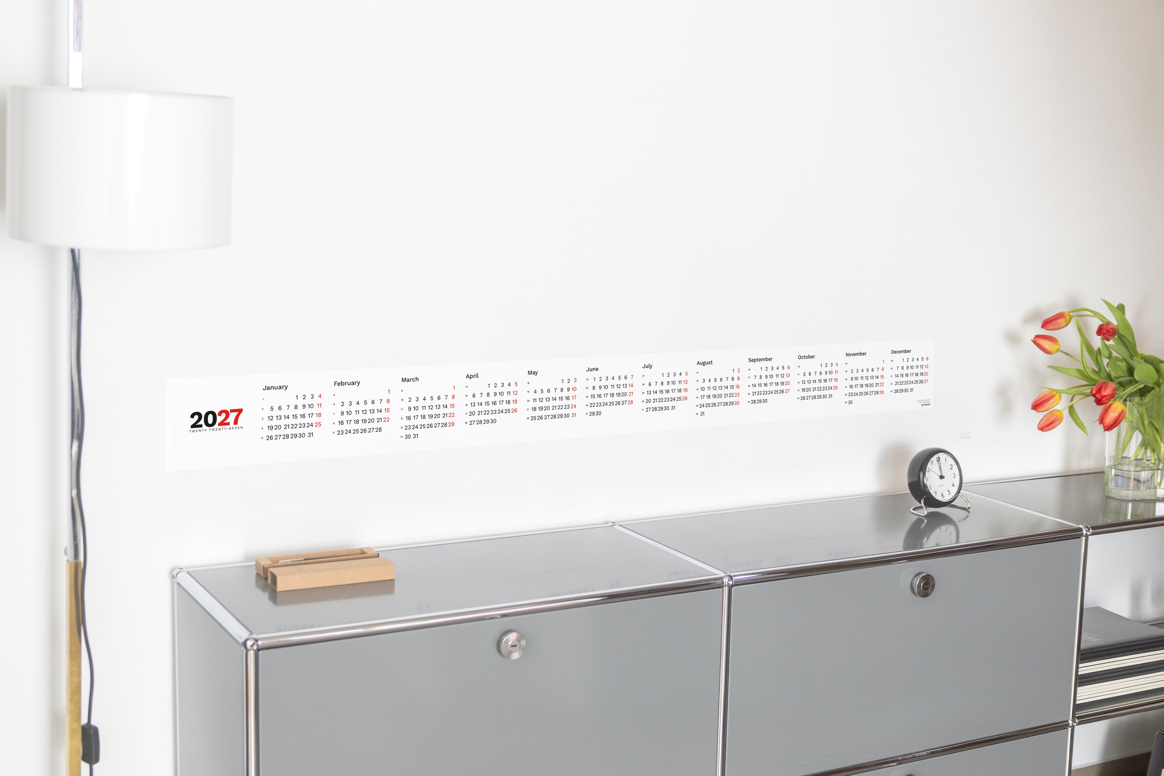 2027 Horizontal Calendar by Octàgon Design. The calendar placed on top of a piece of USM furniture and besides the Arne Jacobsen clock and Mila lamp