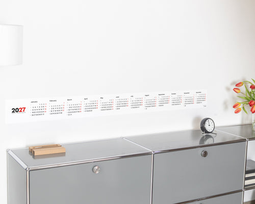 2027 Horizontal Calendar by Octàgon Design. The calendar placed on top of a piece of USM furniture and besides the Arne Jacobsen clock and Mila lamp