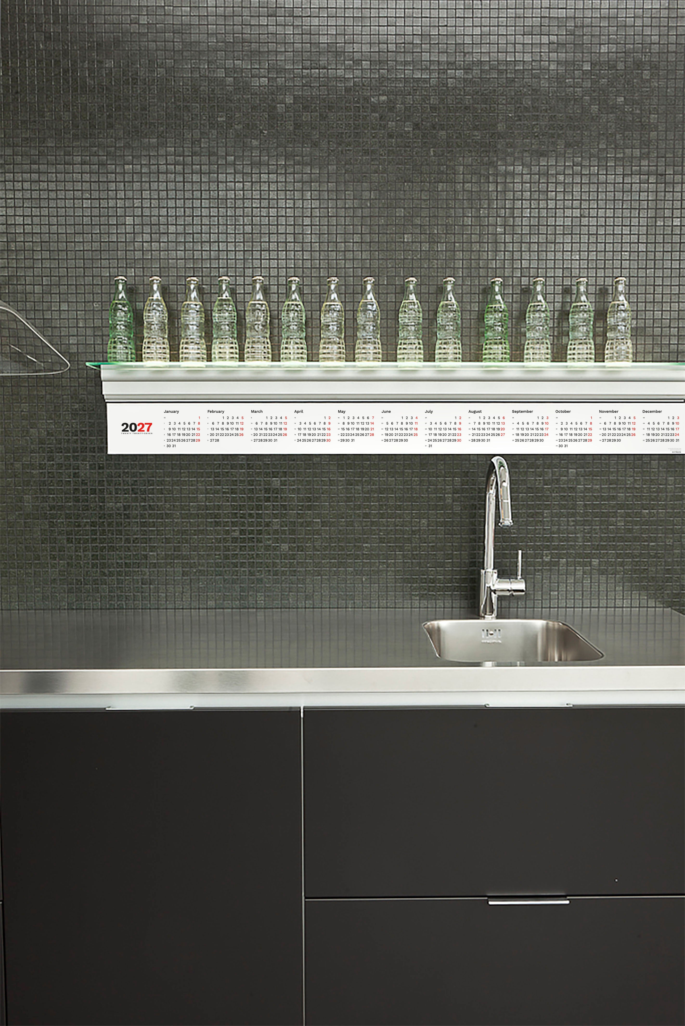 2027 Horizontal Calendar by Octàgon Design. The calendar placed under a bookshelf of a Boffi kitchen.