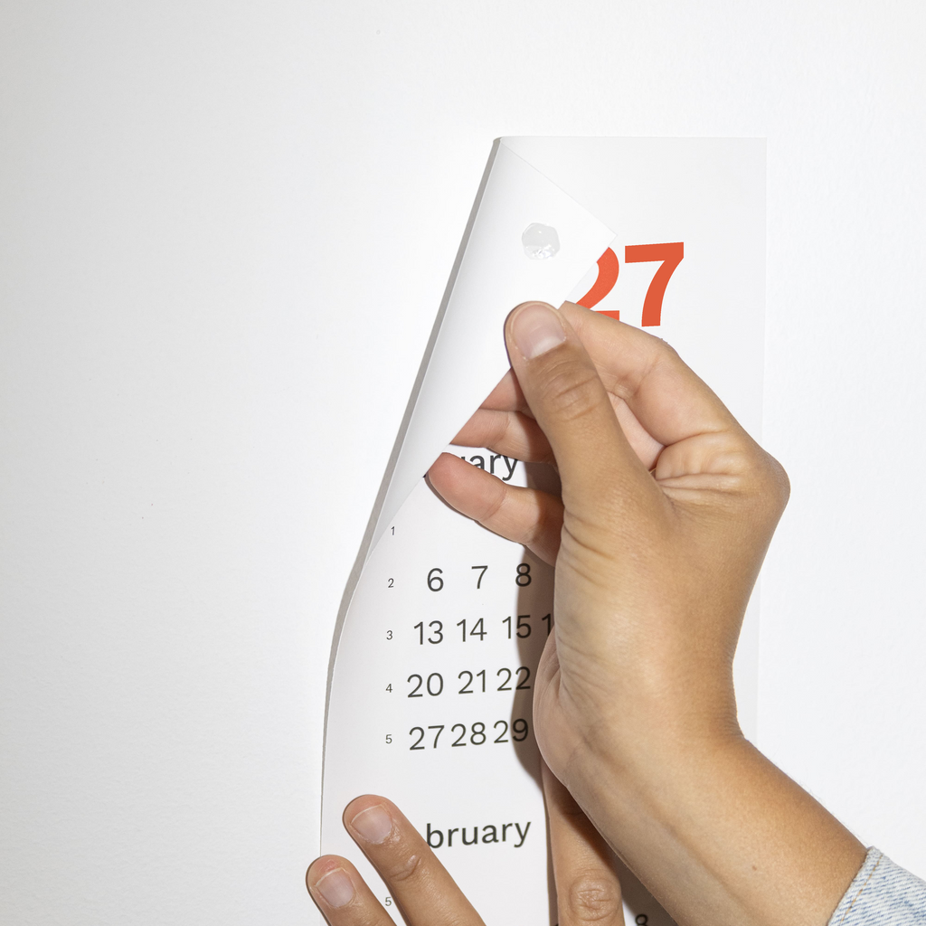 2027 Vertical Calendar by Octàgon Design. A girl hanging the calendar on the wall. 