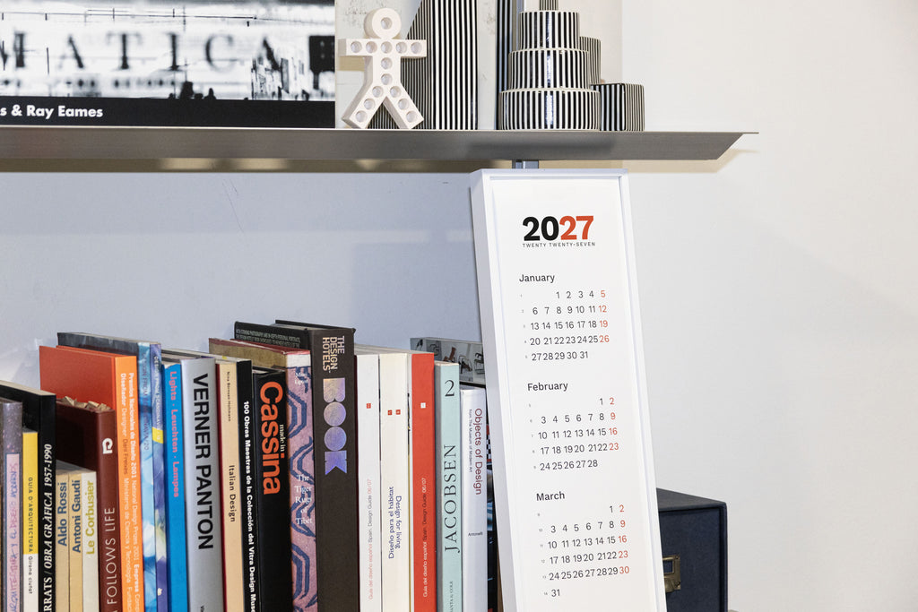2027 Vertical Calendar by Octàgon Design. The calendar in front of a shelf.