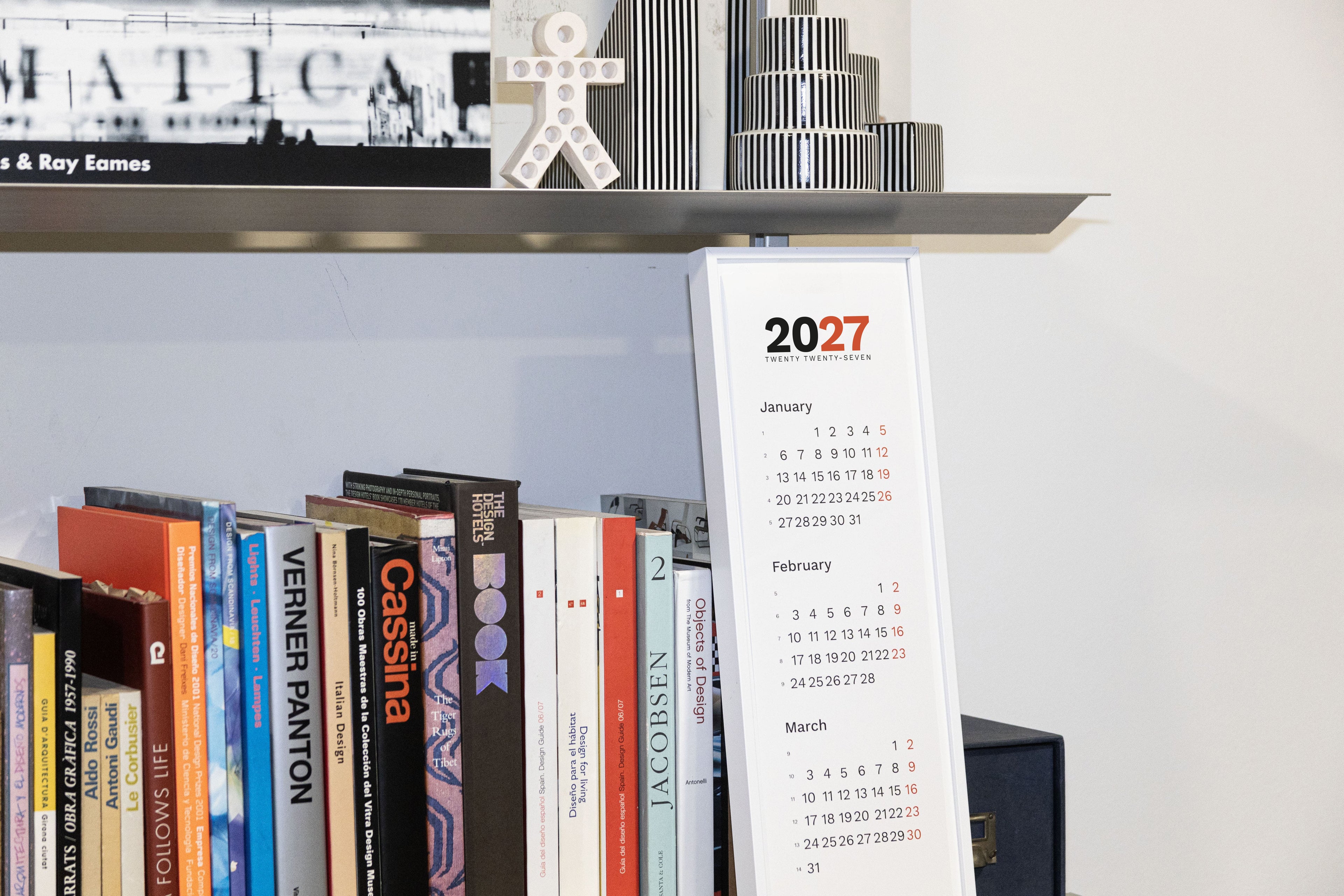 2027 Vertical Calendar by Octàgon Design. The calendar in front of a shelf.