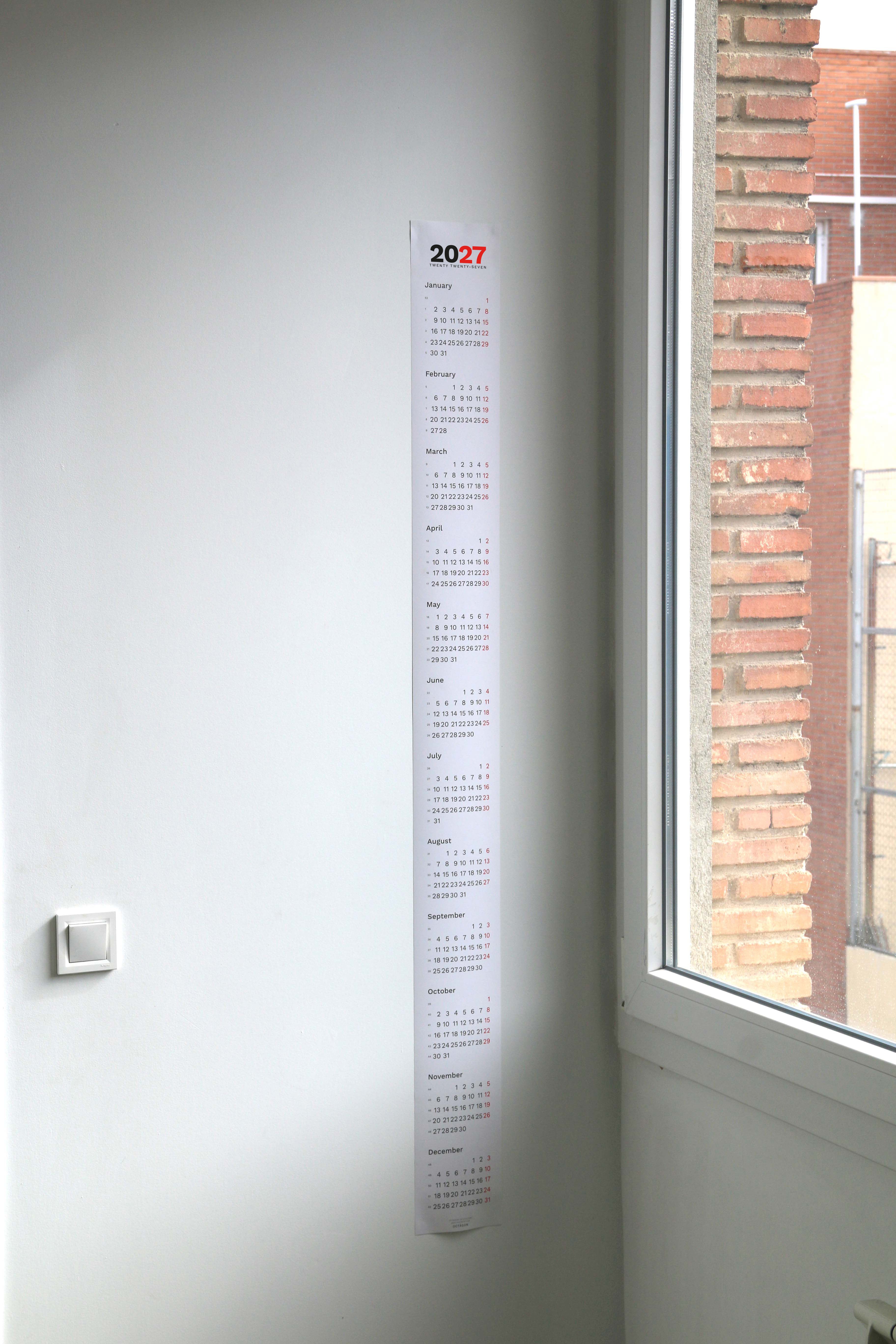 2027 Vertical Calendar by Octàgon Design. The calendar hanging on a wall beside a window.