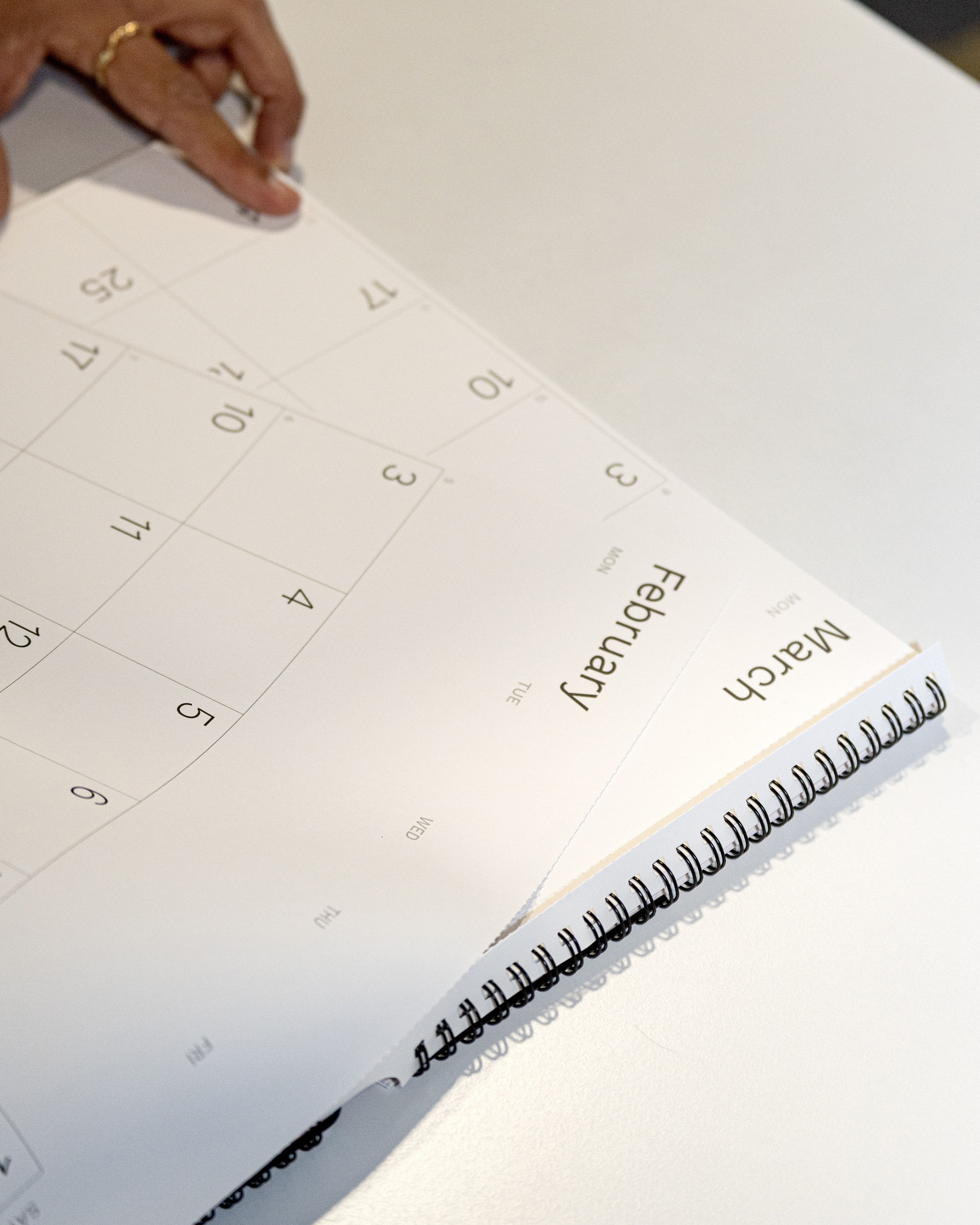 2026 Octàgon Design Wall Planner A3 open to March on a white surface with a hand partially visible.