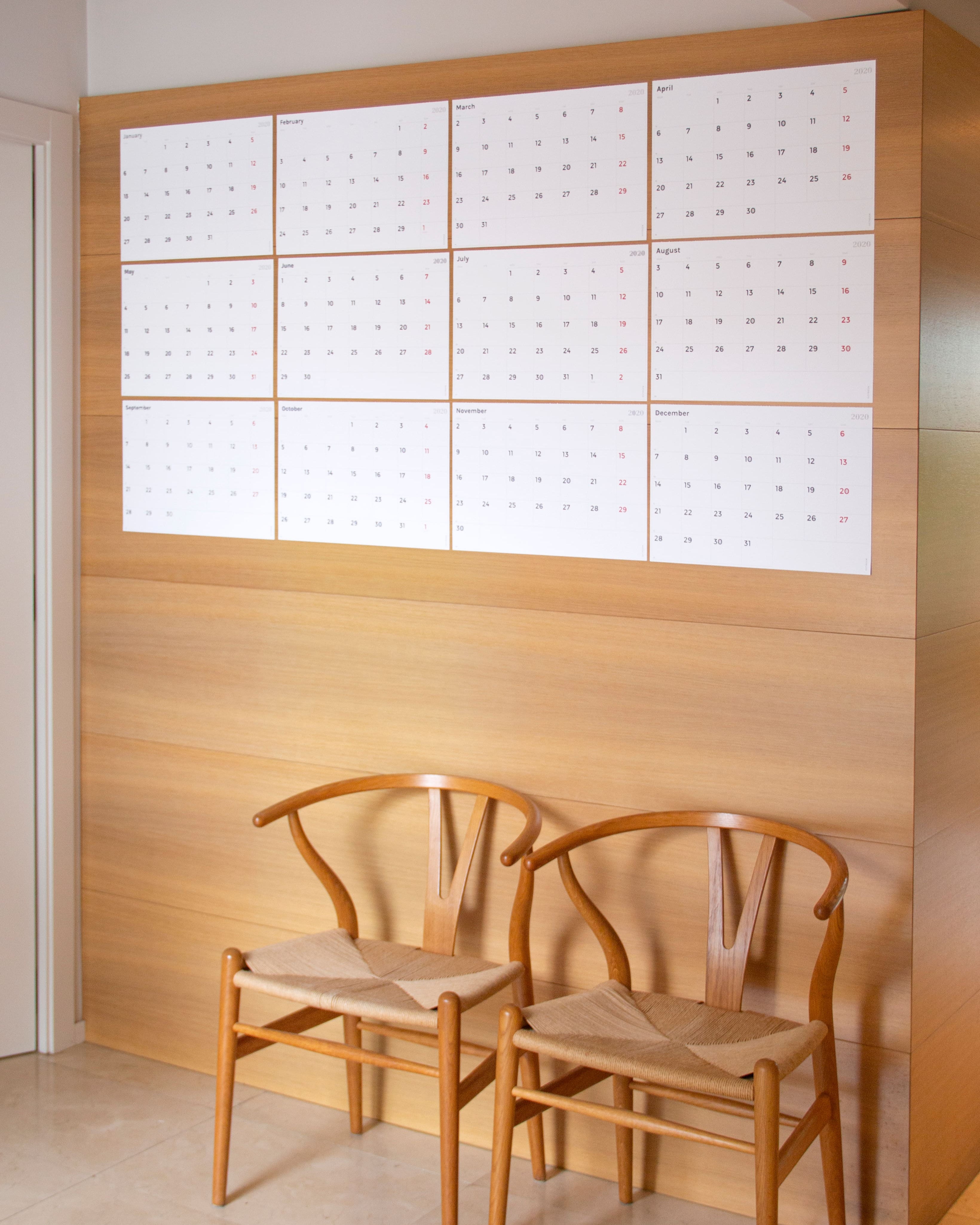 A 2026 Octàgon Design Wall Planner A3 on a wooden wall with two Carl Hansen Wishbone Chairs.