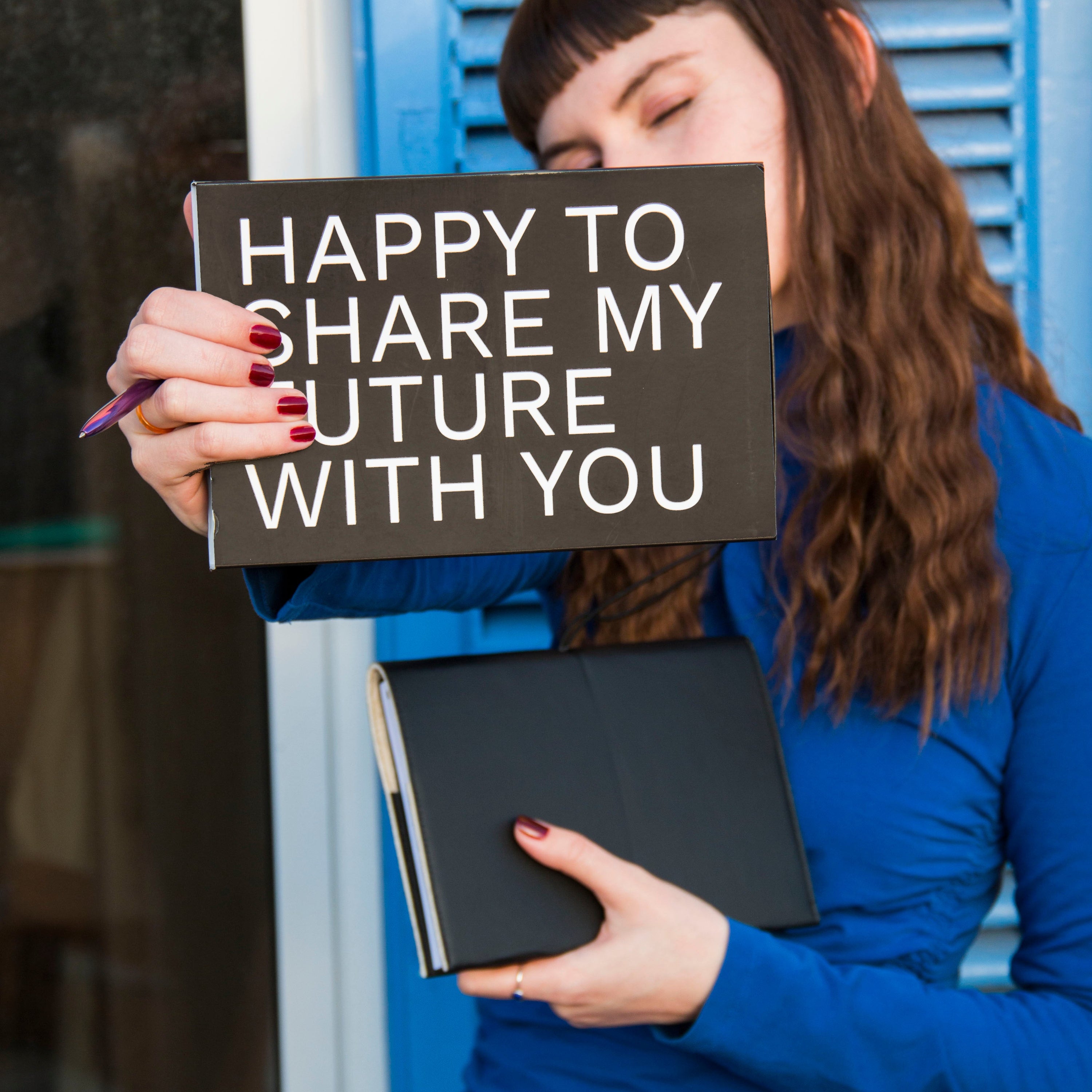Woman holding a gift box and a book with a cover PRO in front of a blue door.