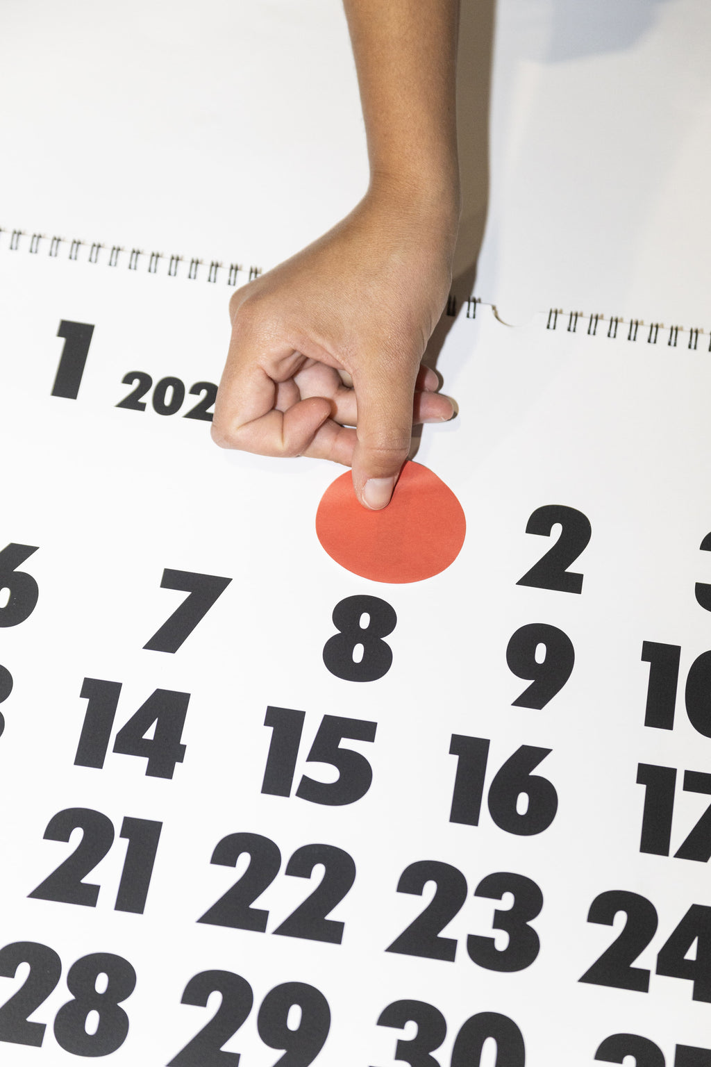 2027 Vinçon wall Calendar by Octàgon Design. A hand putting a round red sticker to mark a date.