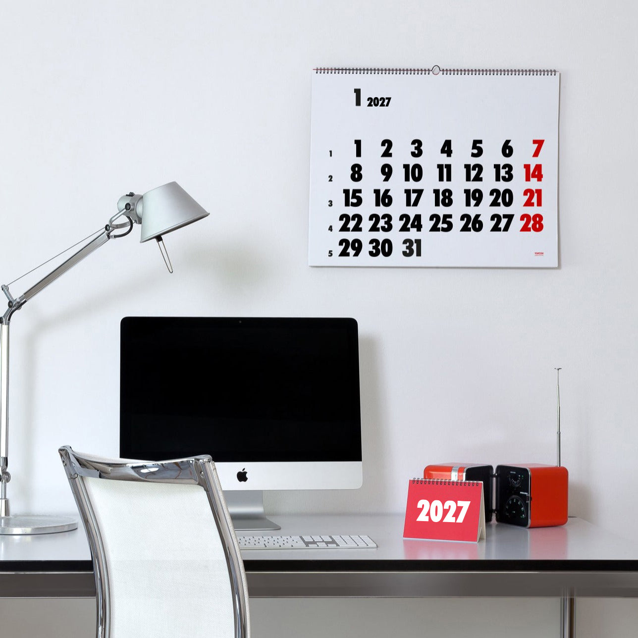 2027 Vinçon wall Calendar by Octàgon Design. The calendar holding on a white wall. Office atmosphere with the Tolomeo lamp, a Apple IMac and a Brionvega radio.