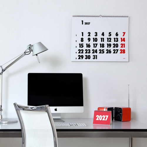 2027 Vinçon wall Calendar by Octàgon Design. The calendar holding on a white wall. Office atmosphere with the Tolomeo lamp, a Apple IMac and a Brionvega radio.
