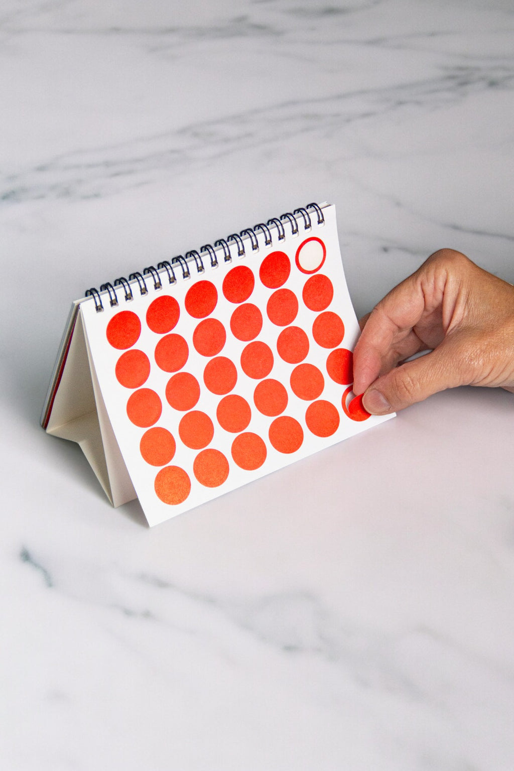 2027 Vinçon desk calendar by Octàgon Design. A hand putting a round red sticker to mark a date.