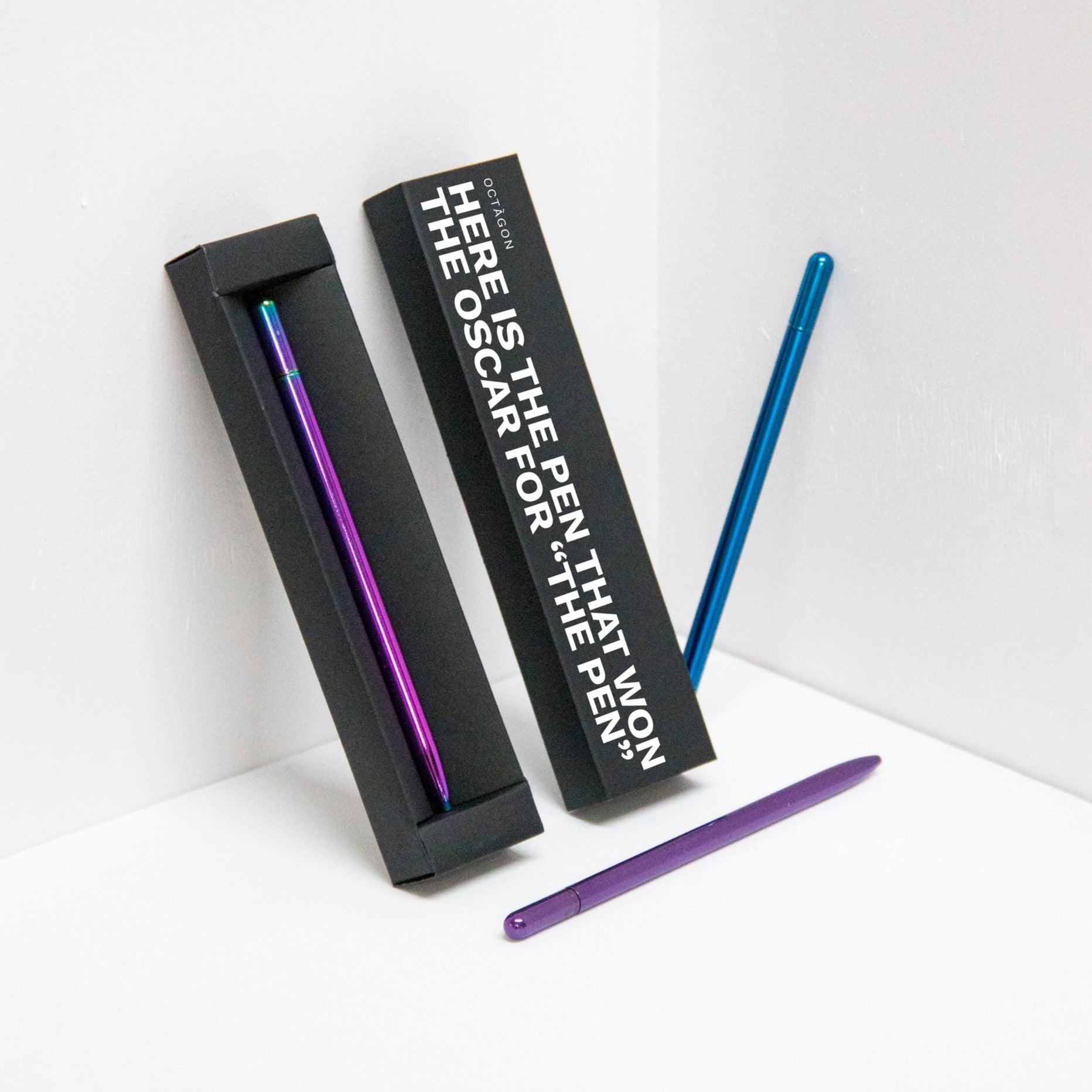 OCTÀGON DESIGN | "Drop Pen" metallics rainbow, purple and blue color pens and black pen box with "Here is the pen that won the Oscar for "THE PEN" print white colour.